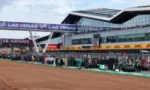 Pit lane at a Las Vegas motorsport race with team garages, crew members, and sponsor banners in the background.