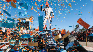 Motorsport race winner on top of a ceremonial car, confetti raining down during a victory celebration.
