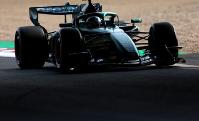 Low-angle shot of a teal Formula 1 car cornering on a sunlit race track, front view and wide tires visible