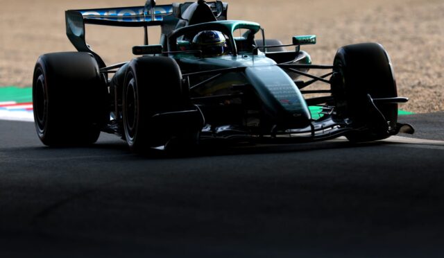 Low-angle shot of a teal Formula 1 car cornering on a sunlit race track, front view and wide tires visible