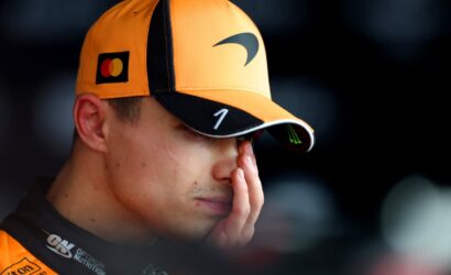 Close-up of a person wearing an orange cap with a MasterCard logo, resting their face in their hand in a tired or contemplative moment.