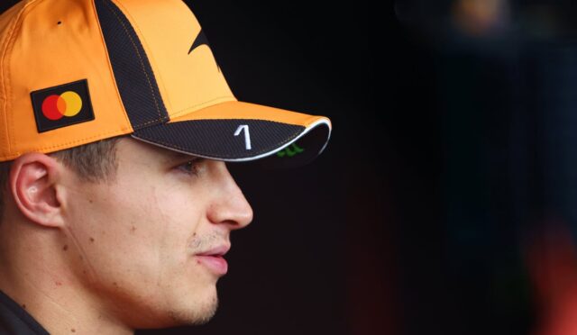 Profile view of a man wearing an orange cap with a Mastercard logo, looking to the right against a dark background prep area.