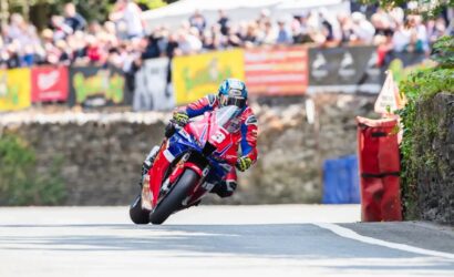 Motorcycle racer leaning into a corner on a road race, bike number 3 amid cheering crowds and barriers in the background.