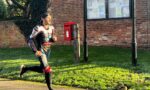Male jogger in a racing suit runs past a brick wall, red post box, and parish council noticeboard labeled 'OSBASTON PARISH COUNCIL'.
