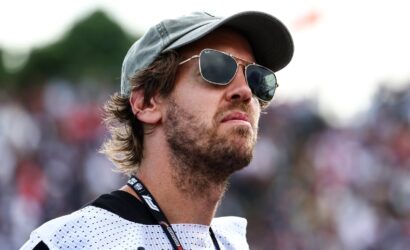 Man wearing a gray cap and sunglasses looking into the distance at an outdoor crowd event