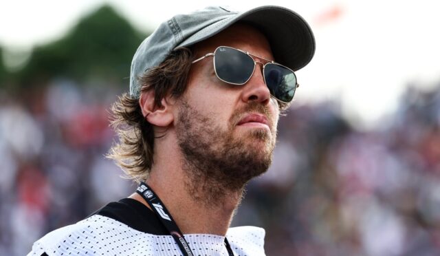 Man wearing a gray cap and sunglasses looking into the distance at an outdoor crowd event