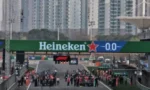 Race cars line up at the start of a street circuit under a Heineken banner and countdown clock, with tall buildings in the background.