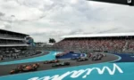 Formula 1 cars racing on a bright blue track with packed grandstands in the background.