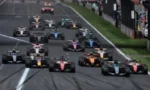 Grand Prix start: a pack of colorful Formula 1 cars lined up on the grid at the start of a race on a paved track.