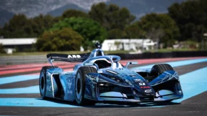 Blue formula-style race car speeding on a blue-and-red racetrack with trees in the background.