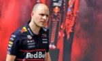 Male race car driver wearing Red Bull team apparel, posing in front of a red sponsor backdrop.