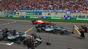 Pit lane at a Formula 1 race with multiple race cars, crew members, Heineken banners along the track, and a packed grandstand.