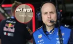 Formula 1 team member in a blue McLaren racing suit wearing a headset, in the pit lane
