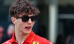 Young man in a red Ferrari team shirt wearing sunglasses, looking to the right.