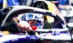 Close-up of a Formula 1 driver wearing a blue helmet inside a race car cockpit, sponsors visible on suit and car.