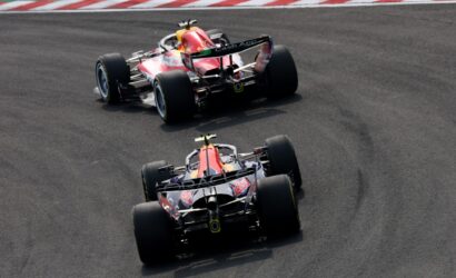 Two Red BullFormula 1 cars chase each other through a sharp right-hand turn on a race track