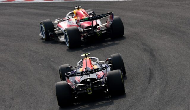 Two Red BullFormula 1 cars chase each other through a sharp right-hand turn on a race track