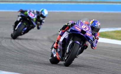MotoGP rider leaning into a turn on a race track; purple bike with sponsor logos.