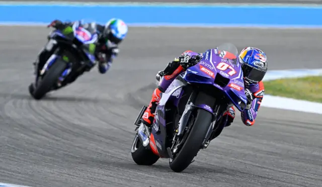 MotoGP rider leaning into a turn on a race track; purple bike with sponsor logos.