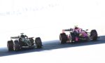 Two Formula 1 cars race side by side on a sunlit track, a dark Mercedes on the left and a pink Racing Point on the right.
