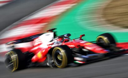Red Formula 1 race car speeding through a corner with motion blur on the wheels and track is visible in the background.