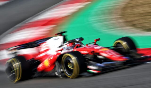 Red Formula 1 race car speeding through a corner with motion blur on the wheels and track is visible in the background.