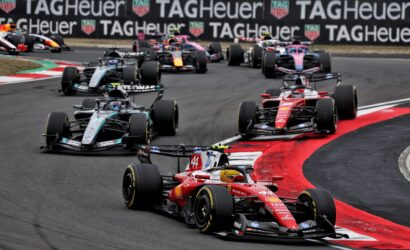Motorsport race: multiple Formula 1 cars cornering on a track with red and white curbs, TAG Heuer banners in the background