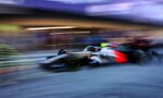 Blurred Formula 1 race car speeding along a track, creating motion streaks and a blue-purple background.