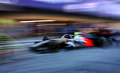 Blurred Formula 1 race car speeding along a track, creating motion streaks and a blue-purple background.