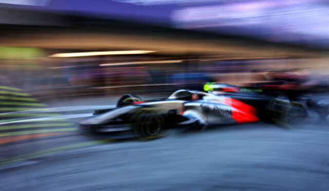 Blurred Formula 1 race car speeding along a track, creating motion streaks and a blue-purple background.