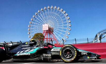 Formula 1 race car with Petronas livery on a racetrack, ferris wheel visible in the blue sky behind it.