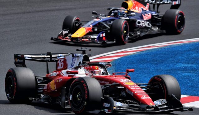 Red Ferrari Formula 1 car leading a race, closely followed by a Red Bull car on a curving track with blue run-off area behind.