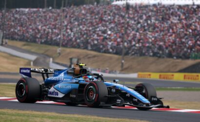 Blue Formula 1 race car sprinting along a track with a packed grandstand in the background