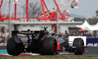 Close-up of a black Formula 1 car with Revolut branding on the rear wing, speeding along a race track with a red-and-white curb in view.