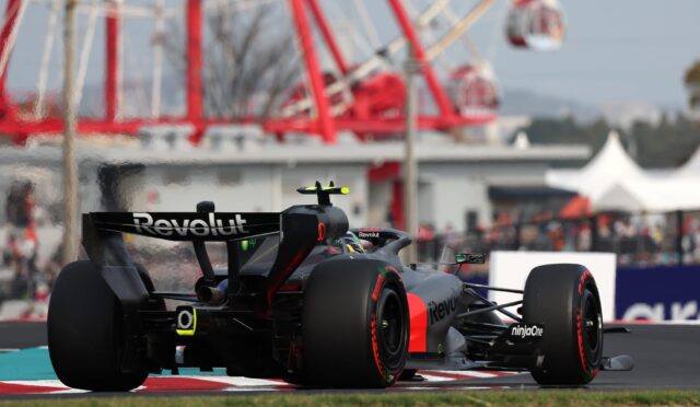 Close-up of a black Formula 1 car with Revolut branding on the rear wing, speeding along a race track with a red-and-white curb in view.