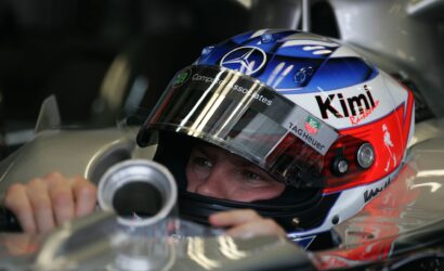 Close-up of a race car driver wearing a colorful helmet, gripping the steering wheel inside the cockpit.