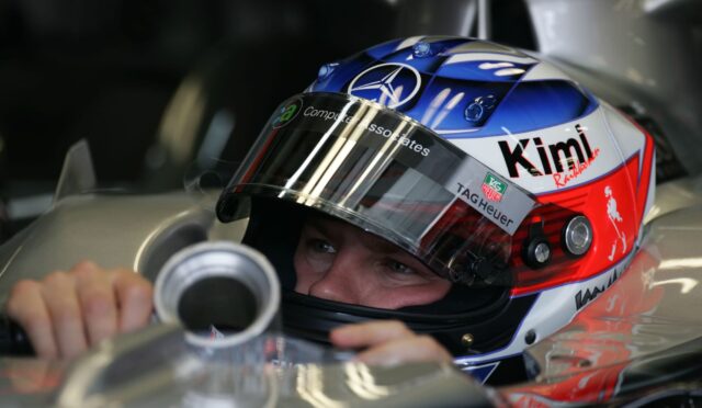 Close-up of a race car driver wearing a colorful helmet, gripping the steering wheel inside the cockpit.