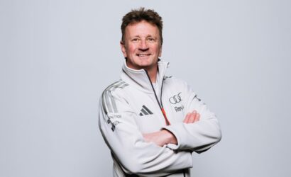 Smiling man in a white athletic jacket with arms crossed, standing in a studio background