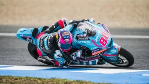 Motorcycle racer wearing turquoise and pink gear leans sharply into a turn on a race track, bike #88 in view.