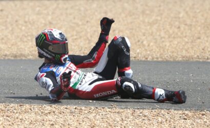 Motorcycle racer in Honda suit crashes and slides on the track, debris and gravel around him.