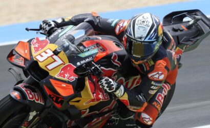 Motorcycle racer leaning into a turn on a red and yellow Red Bull KTM bike, number 37, helmet in racing colors.