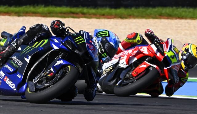 Group of professional motorcycle racers leaning into a tight turn on a race track, blue Yamaha in foreground with Monster Energy branding.