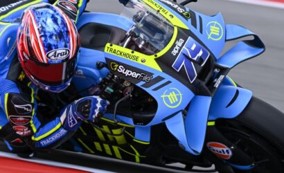 Motorsport rider in blue and yellow suit leaning into a turn on a blue race bike with sponsor logos on the bodywork and helmet.