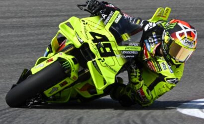 Race motorcycle and rider in neon yellow gear leaning into a sharp turn on a track, full-visor helmet.
