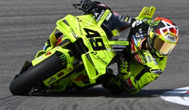 Race motorcycle and rider in neon yellow gear leaning into a sharp turn on a track, full-visor helmet.