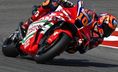 Motorcycle racer in red Castrol livery leaning into a turn, number 10, on a race track.