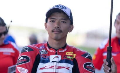 Portrait of a young motorcycle racer in a red Honda racing suit, wearing a blue and white cap, looking at the camera.
