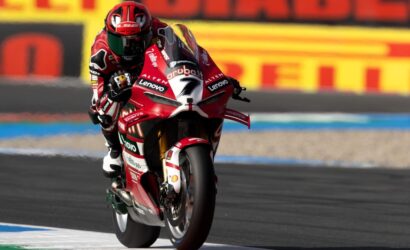 MotoGP rider on a red Ducati motorcycle leaning into a curve on a race track, sponsor logos visible on the bike and suit