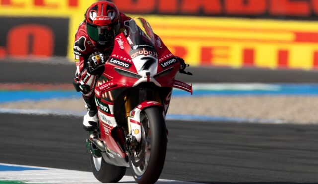 MotoGP rider on a red Ducati motorcycle leaning into a curve on a race track, sponsor logos visible on the bike and suit