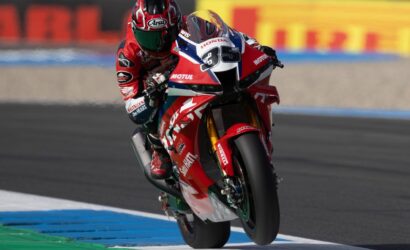 Racing rider in red gear on a red Honda motorcycle leaning into a turn on a race track.